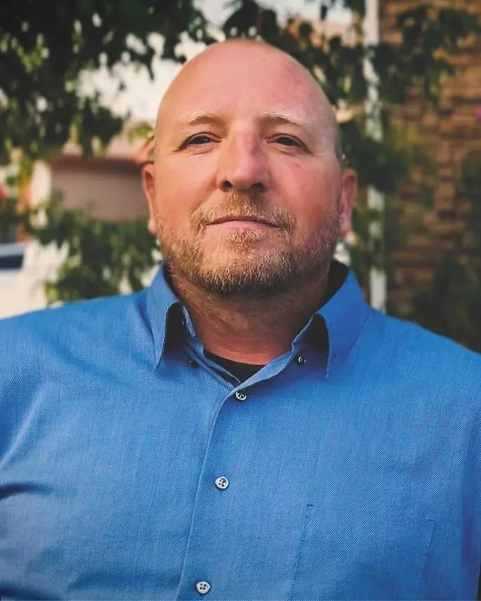 Man in blue shirt outdoors, looking serious.